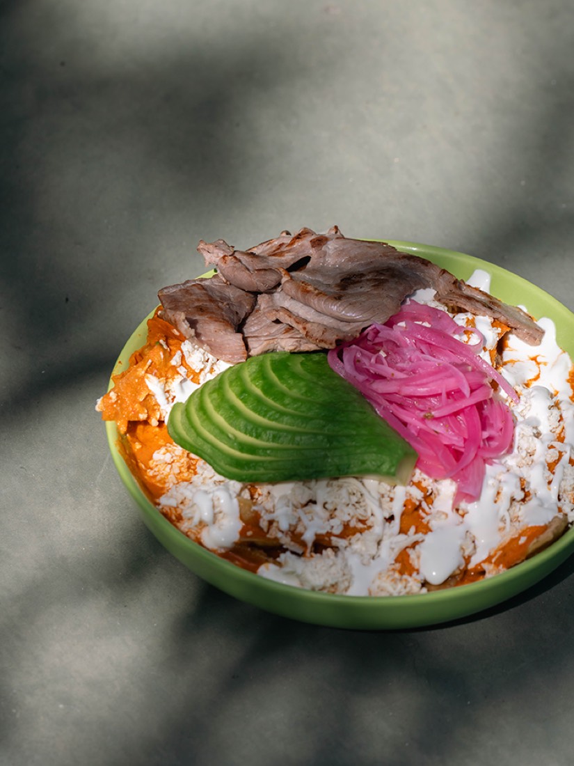 Chilaquiles verdes con cecina, aguacate y cebolla morada en plato verde