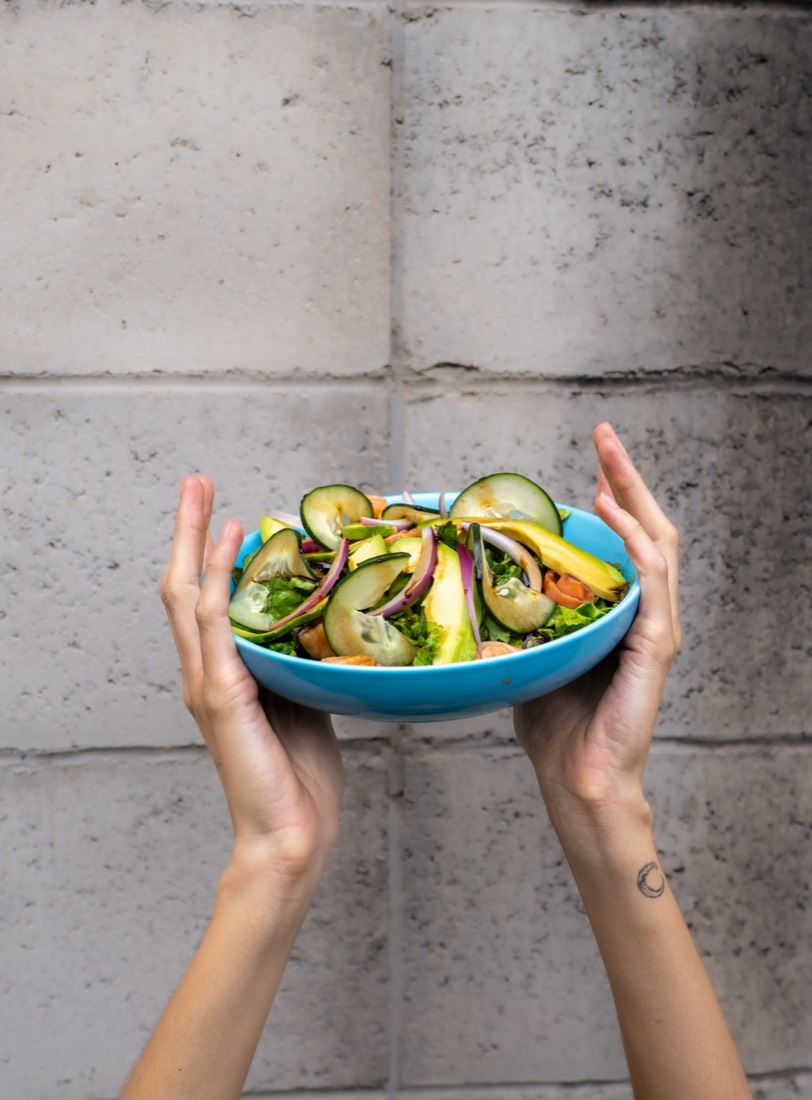 Manos sosteniendo un tazón azul con la ensalada Salmónica